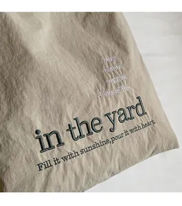 Close-up of the crinkle texture fabric and embroidered lettering on the khaki tote bag
