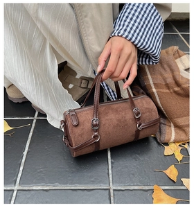 Close-up of brown suede barrel bag with leather handle and silver metal zipper detail
