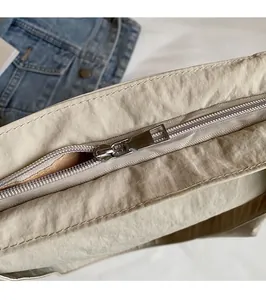 Detailed close-up of smooth silver metal zipper on a beige nylon commuter tote bag