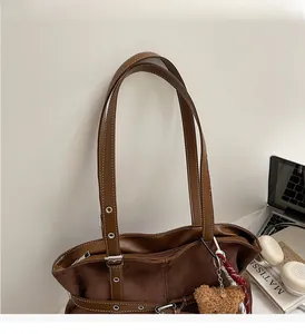 Close-up of retro brown suede tote bag with silver eyelets and plush bear charm