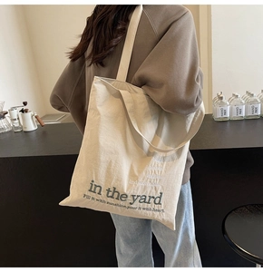 Detail of a beige canvas tote bag with green embroidery being worn over the shoulder