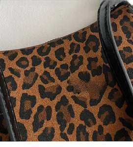 Close-up of leopard print fabric texture and black leather stitching detail on crescent bag