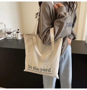 Detail of off-white canvas tote bag featuring green artistic text and botanical print
