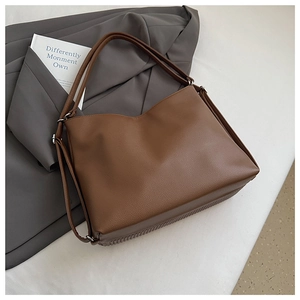 Macro detail of brown pebbled leather tote bag with vertical pleated bottom on a grey suit