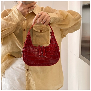 Close-up of vibrant red crescent bag featuring glossy crocodile texture and silver hardware