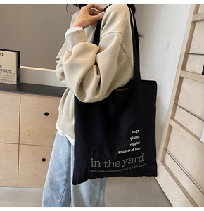 Detail shot of a large black canvas tote bag with white text print on a female model