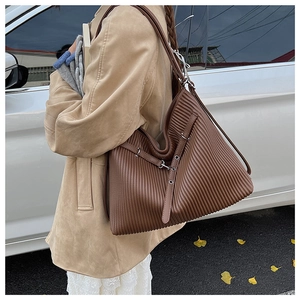 Detailed view of the vertical pleated texture and leather buckle on a dark brown tote bag