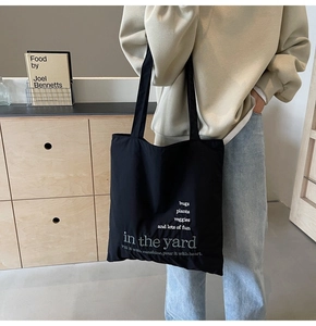 Macro view of black nylon tote bag featuring white minimalist text and double straps