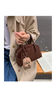 Detail der Wildleder-Handtasche mit Ledergriffen und Plüschbär-Anhänger im Freien