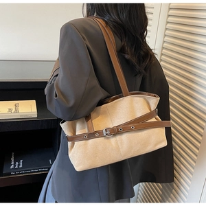 Detail of beige tote bag with brown leather accents and slim shoulder strap