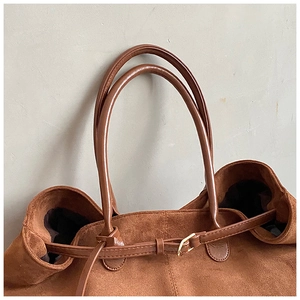 Detailed close-up of brown suede tote bag with smooth leather strap and gold buckle