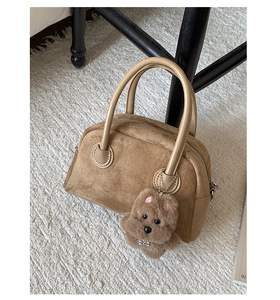 Detail einer braunen Wildleder Boston Tasche mit Ledergriffen und Plüschtier-Anhänger