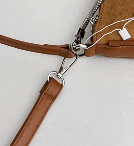 Detail of silver metal lobster clasp and suede texture on a camel shoulder bag