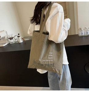 Olive green canvas tote bag with garden embroidery shown on shoulder in a cafe setting