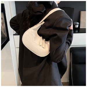 Close-up of white crocodile pattern crescent underarm bag worn over a black blazer