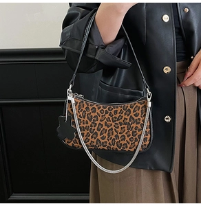 Detail of leopard print underarm bag with black trim, silver chain, and floral charm