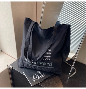Detail of a black canvas tote bag with white lettering against minimalist home decor