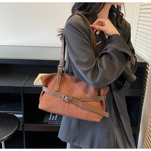 Detail of a brown suede tote bag featuring a leather strap and metal buckle on a shoulder