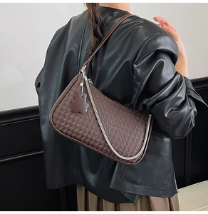 Close-up of brown woven shoulder bag with silver chain strap and bear charm on model