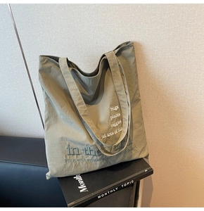Detail of olive green tote bag with embroidered letters on textured canvas fabric