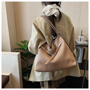 Detail of khaki pleated tote bag featuring vertical accordion texture and wide shoulder strap