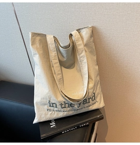 Detailed view of 'in the yard' embroidery on a large beige canvas tote bag surface