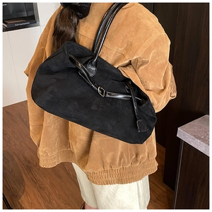 Detail of a black suede tote bag with golden buckle accents worn on the shoulder