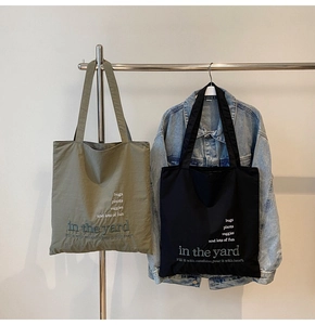 Detail of minimalist canvas tote bags in olive green and black hanging on a metal rack