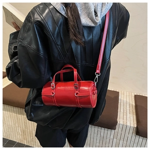 Detail view of shiny red cylinder shoulder bag on black leather jacket outfit