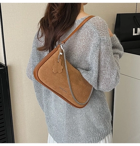 Detailed side view of a brown suede underarm bag with a cute bear charm and silver chain
