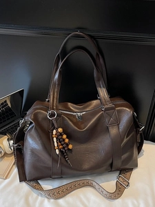 Grand sac à main marron foncé avec bandoulière tissée et perles sur un lit blanc