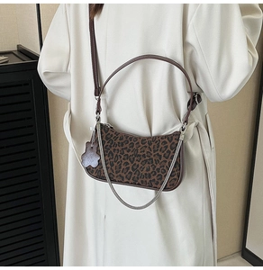 Detail of leopard print crescent bag with silver chain and floral charm on a trench coat