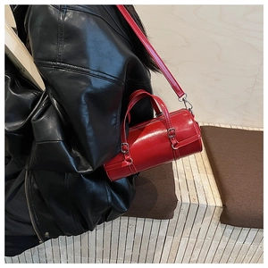 Close-up of red cylinder shoulder bag with metal buckles and detachable strap on a model