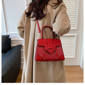 Detail of red floral embossed handbag with gold hardware and removable shoulder strap