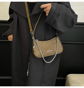 Close-up of khaki crescent bag with metal chain detail on a black trench coat