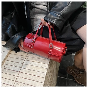 Detailed view of red cylinder bag with silver buckles held by a model in leather jacket
