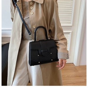 Chic black embossed handbag with gold rivets held by a model in a trench coat