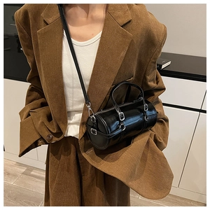 Chic black glossy cylinder bag styled with a brown blazer and silver hardware details