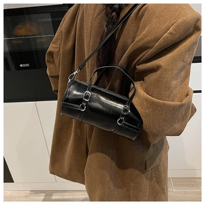 Detail of a black cylinder bag with silver metal buckles on a brown corduroy blazer