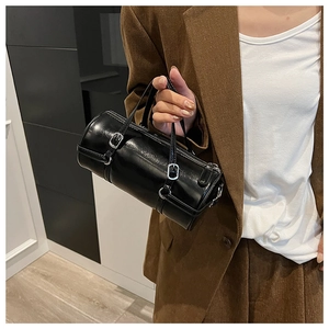 Detail of a black glossy cylinder handbag with silver buckles and leather straps