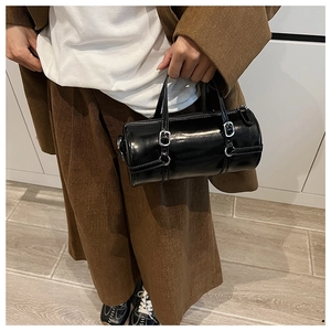 Detail of a black cylinder handbag featuring glossy PU leather and silver metal hardware