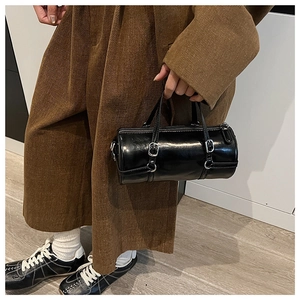 Chic black cylinder bag shown with corduroy outfit and silver hardware details