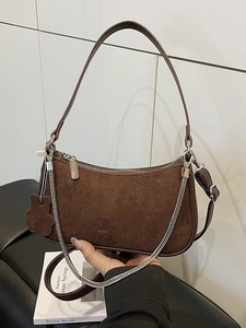 Brown suede crescent underarm bag with silver chain and floral charm on white tile background