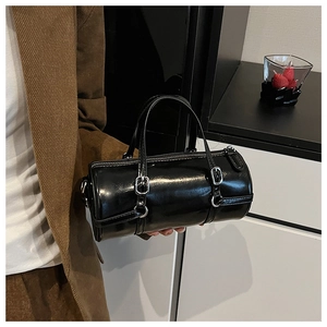 Close-up of black glossy PU cylinder bag featuring decorative silver buckle straps