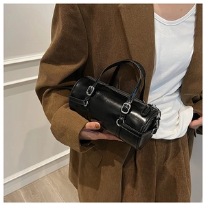 Fashionable black cylinder handbag with silver buckles held by a model in a brown suit