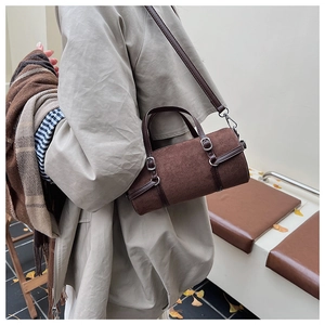Close-up of brown suede barrel bag with silver hardware and leather strap in autumn setting