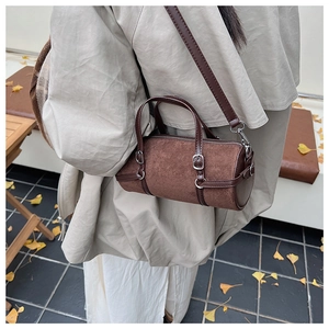 Brown suede cylinder bag with silver hardware worn by a model in autumn scenery