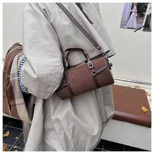 Deep brown cylindrical PU bag with suede texture and metal buckle detail worn over a trench coat