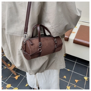 Brown suede cylinder bag shown on shoulder with autumn leaves background detail