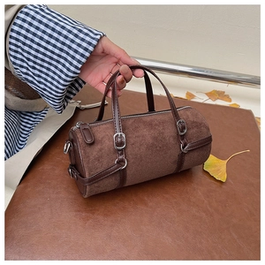 Detail of dark brown cylindrical handbag in suede finish with autumn leaf backdrop